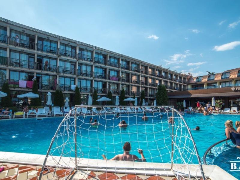Buitenzwembad met waterpolotor voor een meerhoog hotel bij een heldere blauwe lucht.
