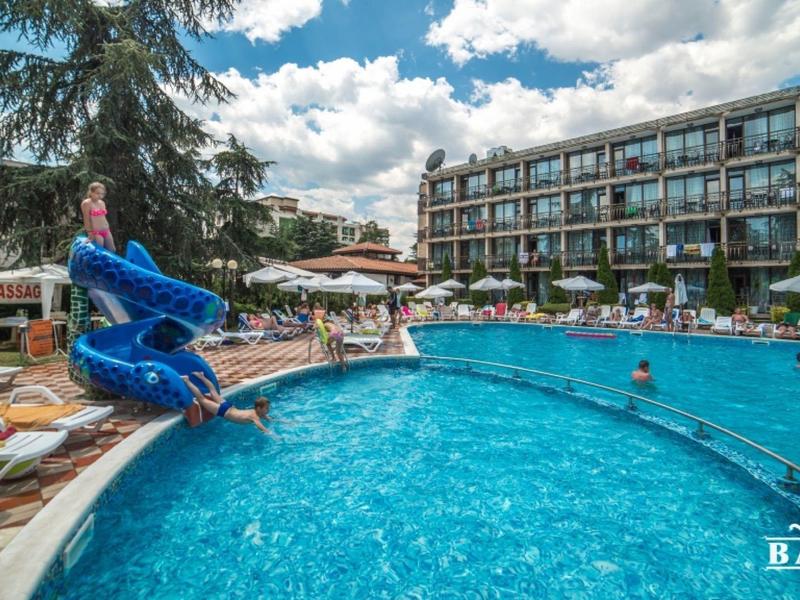 Hotelzwembad met glijbaan, ligstoelen en gasten bij zonnig weer.