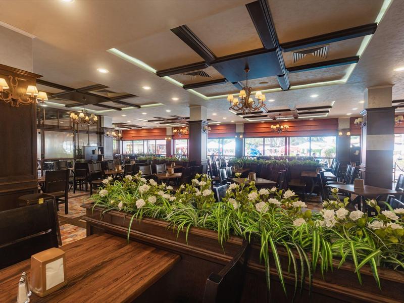 Ruime, elegante hotelrestaurant met groene planten en houten meubels.