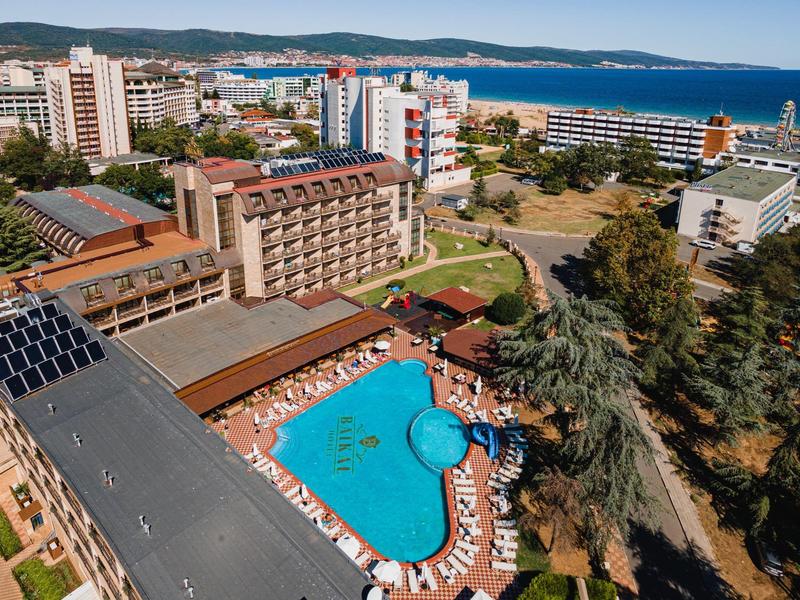 Hotelcomplex met groot buitenzwembad, ligbedden en uitzicht op de zee in de verte.