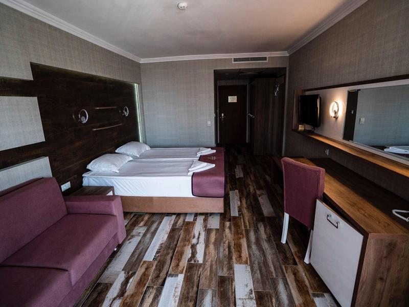 Modern hotelkamer met tweepersoonsbed, bank, bureau en houten vloer.