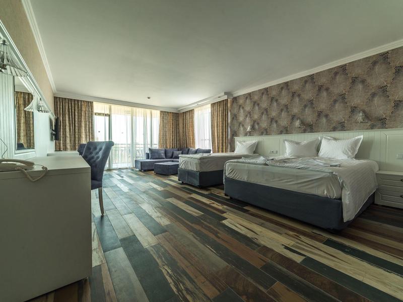 Lichte hotelkamer met twee tweepersoonsbedden, moderne houten vloer en zithoek bij het raam.