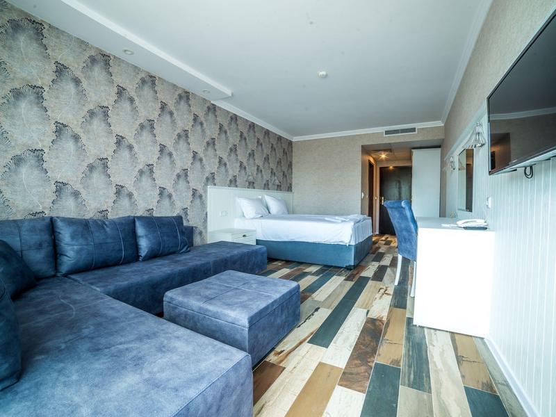 Moderne hotelkamer met tweepersoonsbed, donkerblauwe bank en patroon houten vloer.