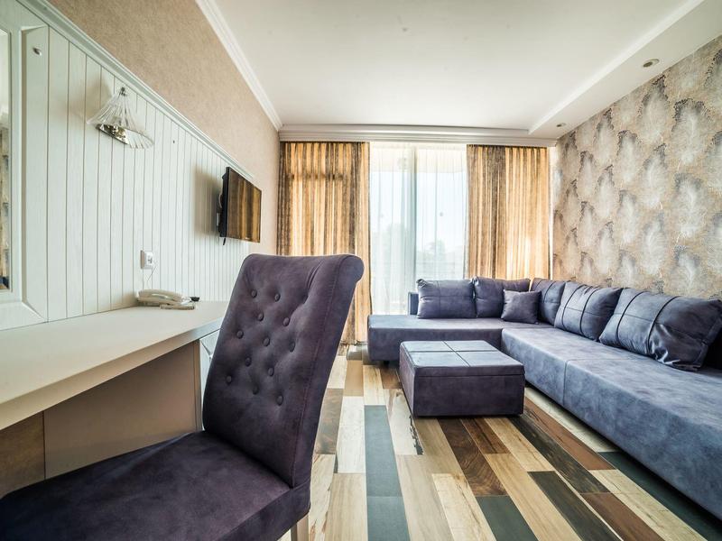 Lichte woonkamer met grijze bank, tapijt en bureau met stoel.