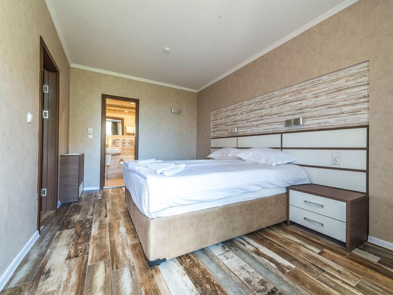 Eenvoudige hotelkamer met tweepersoonsbed, houten vloer en moderne inrichting.