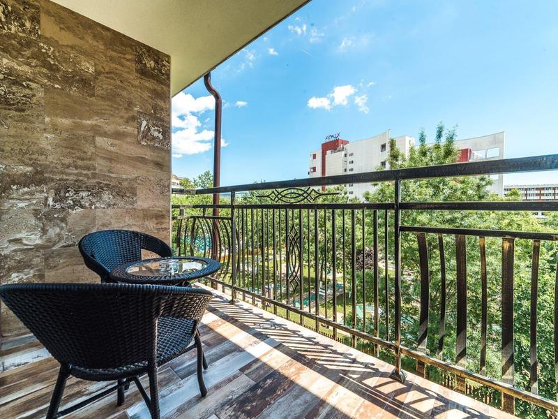 Balkon met twee zwarte stoelen en tafel, uitzicht op bomen en gebouwen onder blauwe lucht.
