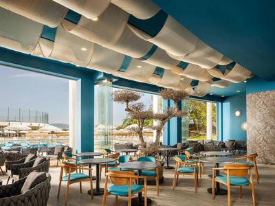 Moderna sala de hotel con paredes azules, sillas de madera y grandes ventanas con vista al exterior.