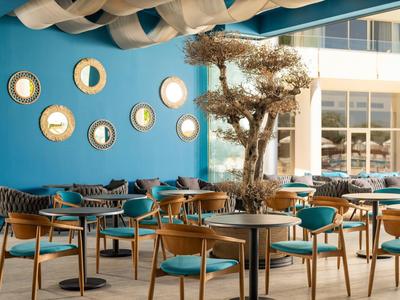 Área de asientos exterior moderna con paredes azules, espejos y sillas de madera bajo un toldo azul.