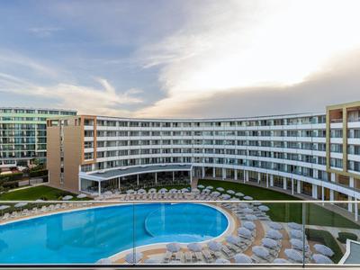 Nowoczesny hotel z okrągłym basenem i leżakami pod pochmurnym niebem.