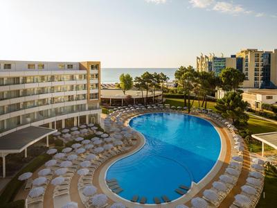 Duży zakrzywiony basen z wieloma leżakami w hotelu pod bezchmurnym niebem.