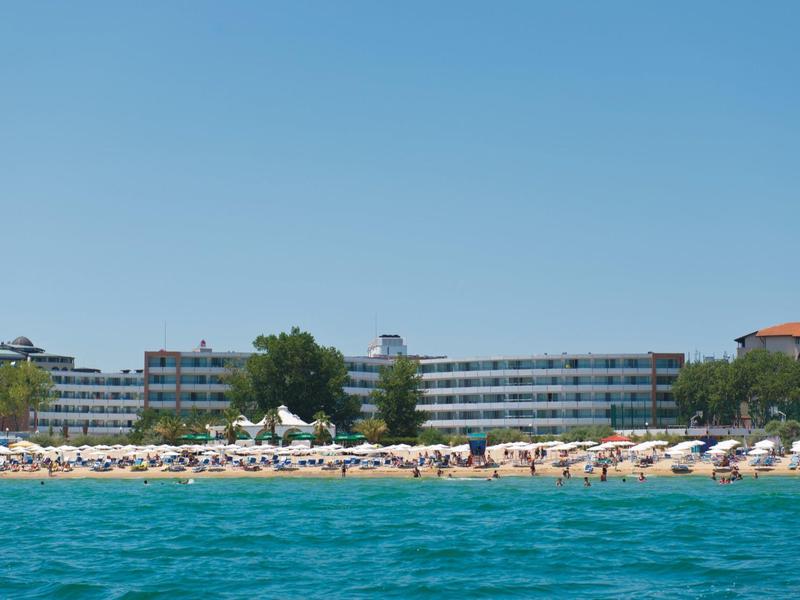 Edificio del hotel en una playa con muchas sombrillas y mar azul en primer plano