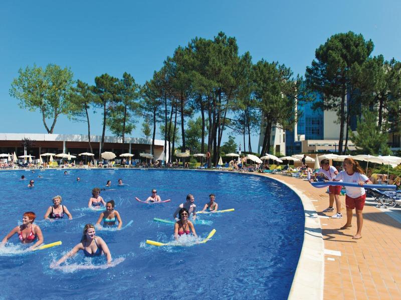 Personas disfrutan de la piscina con tablas y sol en un complejo hotelero.