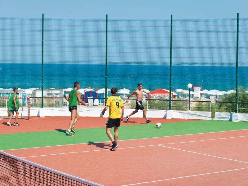 Cuatro personas juegan al fútbol en una cancha junto a la playa con el mar de fondo.