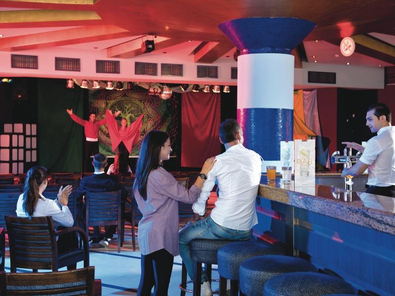 Zona de bar con bartender y personas sentadas y conversando en la barra y en taburetes