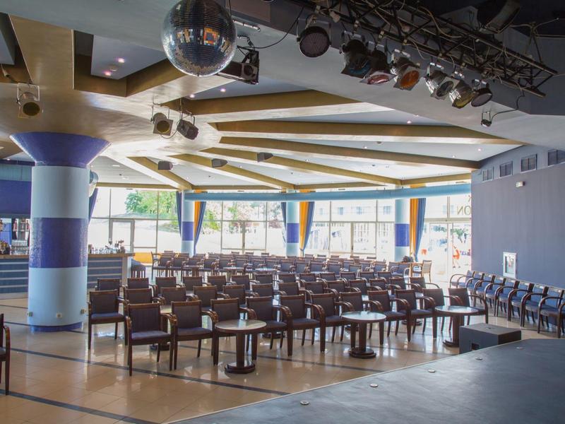 Amplio espacio para eventos con filas de sillas y mesas, iluminado por grandes ventanas.