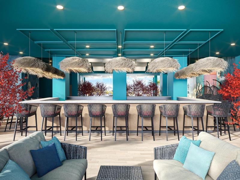 Área de bar moderna con taburetes, paredes azules y asientos al frente en un hotel.