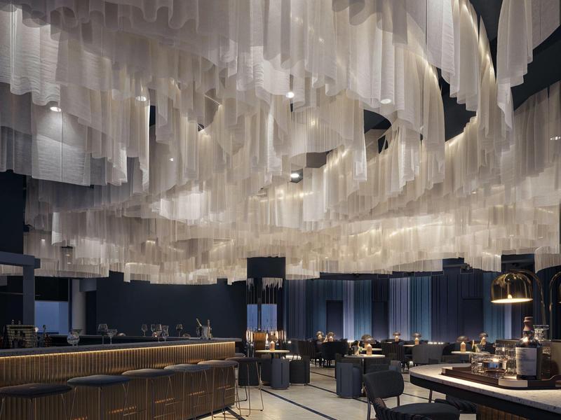 Moderno comedor de hotel con instalación de luces colgantes única y mobiliario elegante.
