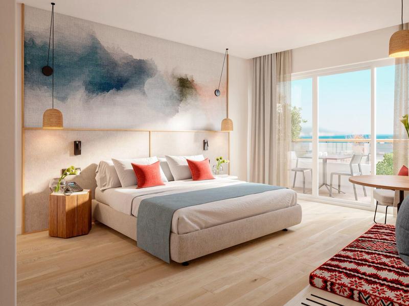 Habitación de hotel moderna con cama grande, arte abstracto en la pared y balcón con vista al mar.