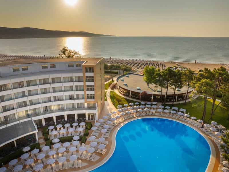 Hotel con gran piscina al aire libre, terraza con mesas y sillas, vista al mar al atardecer