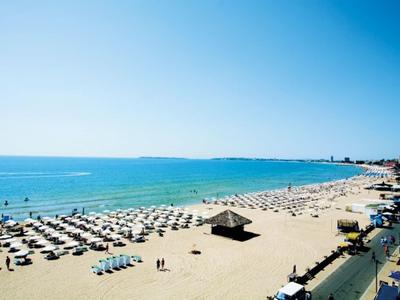 Ampia spiaggia di sabbia con ombrelloni, mare blu chiaro e passeggiatori con tempo soleggiato.