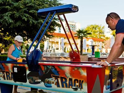 Due persone giocano a calcio balilla colorato all'aperto con alberi sullo sfondo.