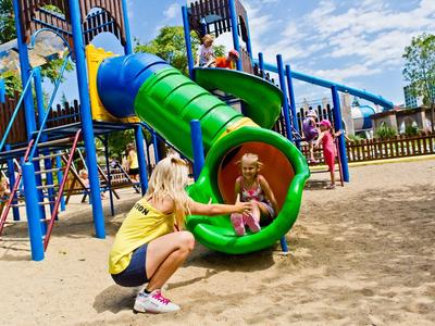 Kinderen spelen op een kleurrijke speeltuin met glijbaan onder een blauwe lucht.