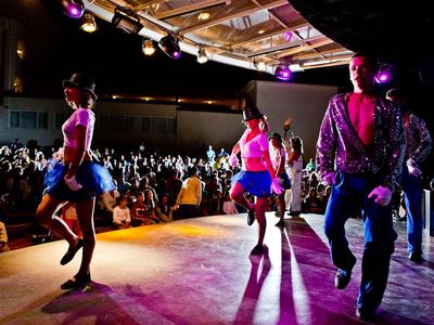 Persone che ballano su un palco davanti a un grande pubblico in una sala eventi.