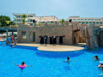 Persone che nuotano in una piscina davanti a un palco con attori vestiti di nero.