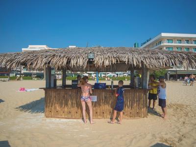 Strandbar aus Bambus mit Strohdach und Kindern davor, Hotel im Hintergrund