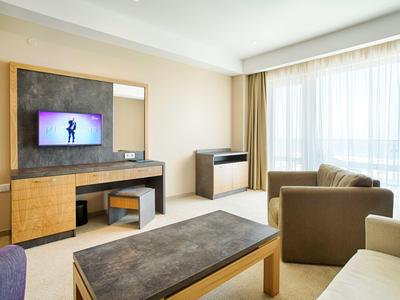 Moderne hotelkamer met bank, aan de wand gemonteerde tv en groot raam met gordijnen.