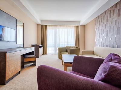 Moderne hotelkamer lounge met zithoek, bureau en groot raam met gordijnen.