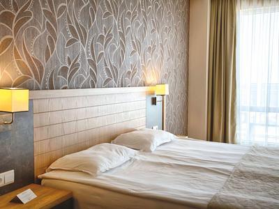 Lichte hotelkamer met twee eenpersoonsbedden, modern houten hoofdeinde en groot raam met gordijnen.