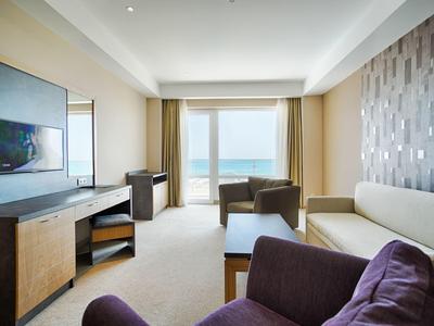 Lichte hotelkamer met zeezicht, bank, fauteuils en flatscreen-tv.