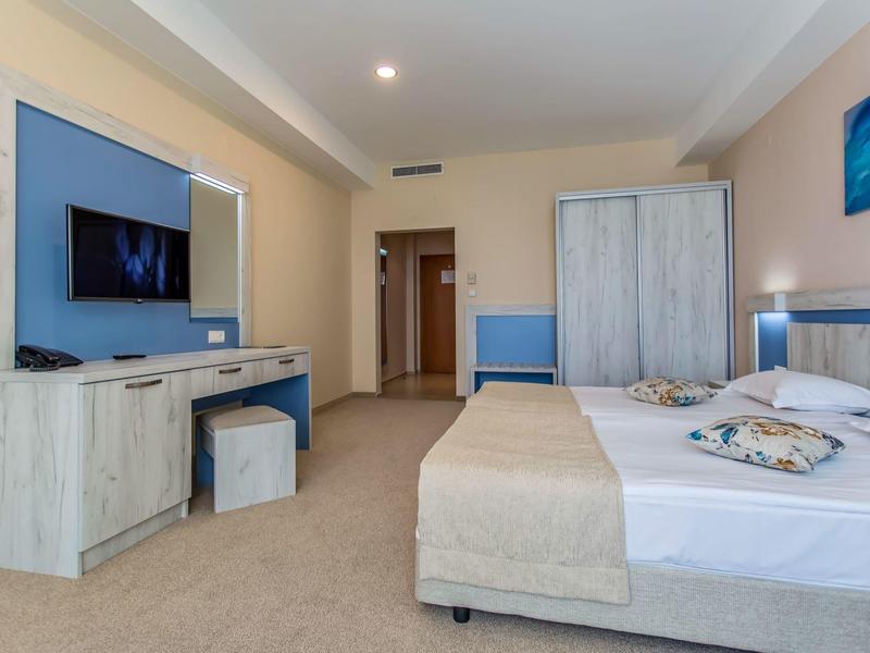 Modern hotelkamer met tweepersoonsbed, flatscreen-tv en kast in lichte kleuren.