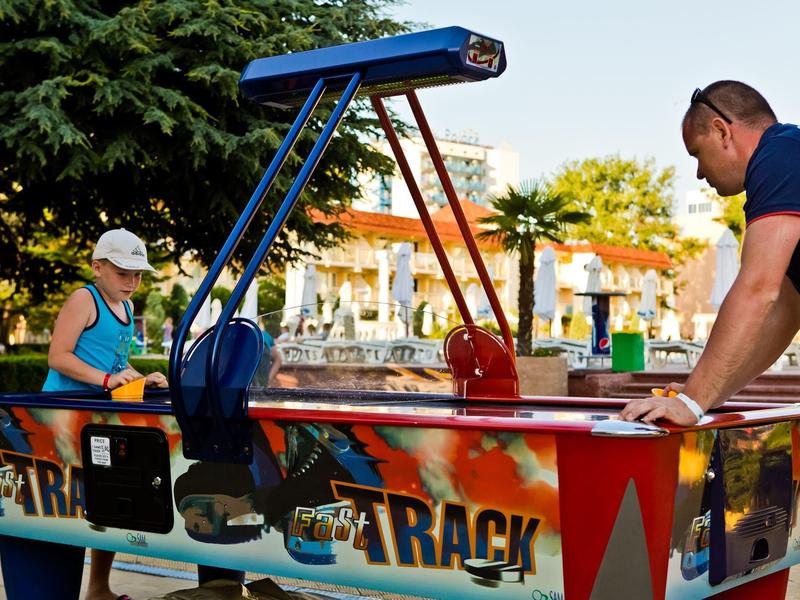 Twee personen spelen airhockey buiten met bomen en gebouwen op de achtergrond.