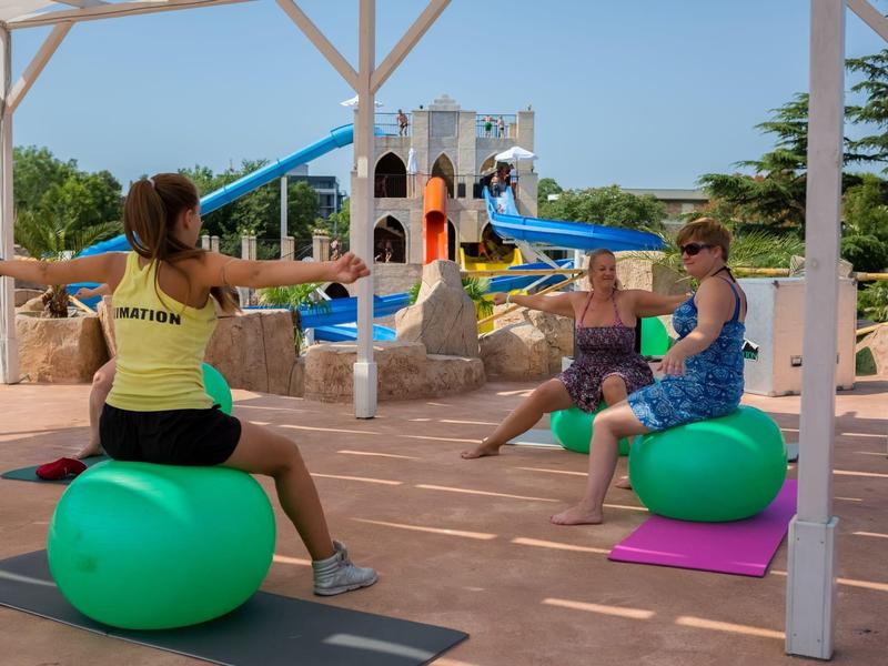Twee vrouwen doen yoga-oefeningen met fitnessballen bij het zwembad in een vakantieoord.