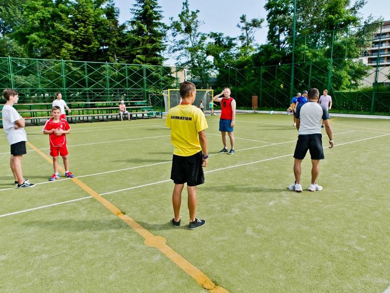 Groep mensen op een buiten sportveld in de zomer, omgeven door bomen en gebouwen.