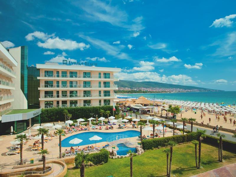 Hotel met zwembad, parasols en tuin direct aan het strand bij zonnig weer.