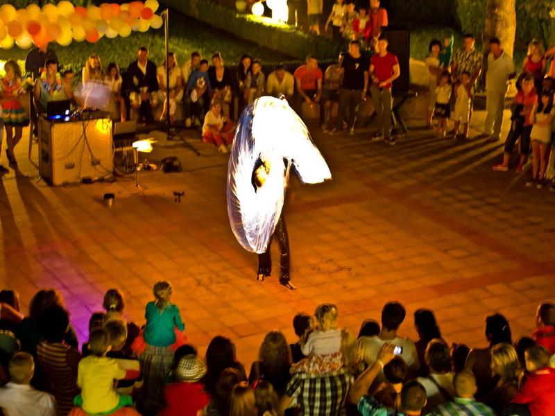 Straatartiest danst in wit kostuum voor publiek bij een buitenfeestelijke gebeurtenis.