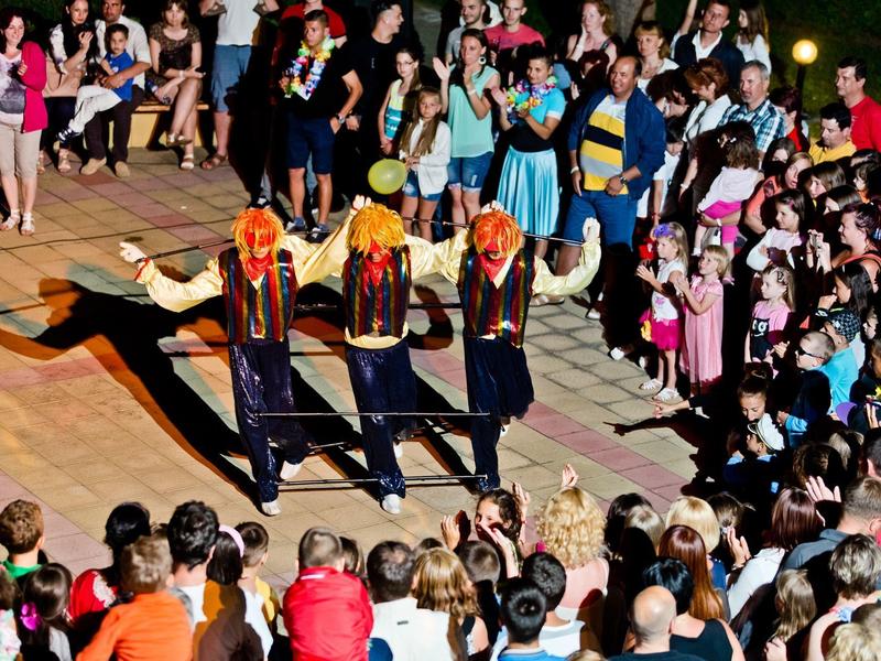 Drie dansers met oranje hoofddoeken voeren een traditionele dans uit voor een grote menigte buiten.
