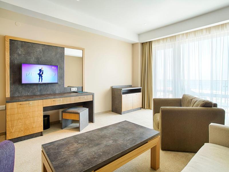 Moderne hotelkamer met bank, aan de wand gemonteerde tv en groot raam met gordijnen.