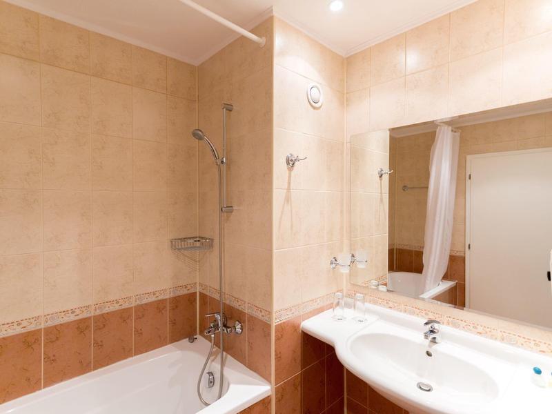 Lichte badkamer met bad, douche en dubbele wastafels in beige en bruine tinten.