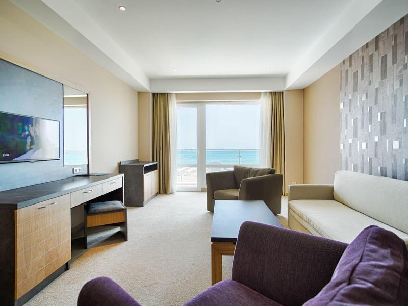 Lichte hotelkamer met zeezicht, bank, fauteuils en flatscreen-tv.