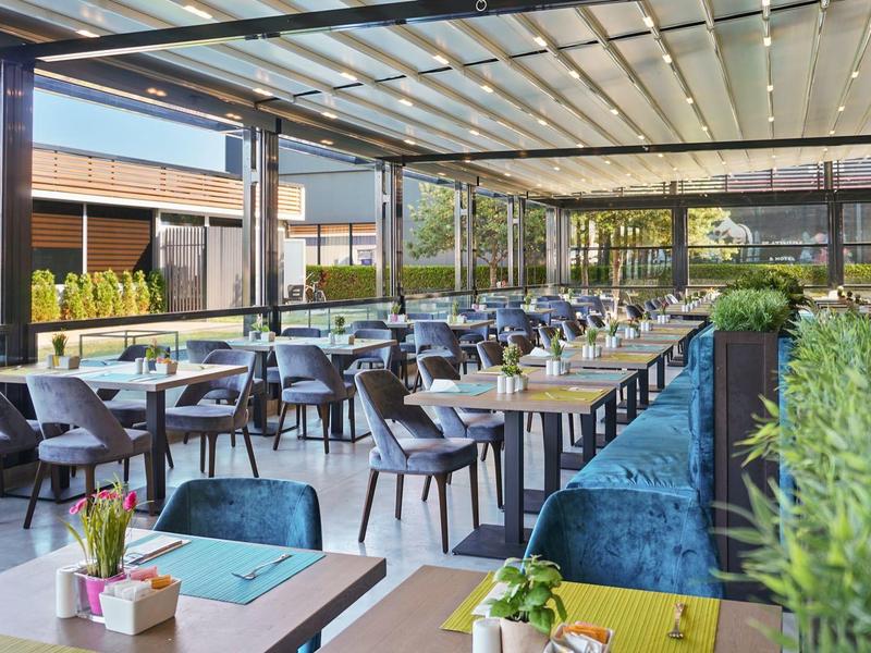 Modern overdekt restaurant met rijen tafels en groene planten.