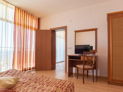 Bright hotel room with window, orange curtains, desk, chair, and wardrobe.