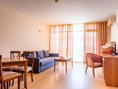 Bright living room with sofa, dining table, chairs, and large window with curtains.