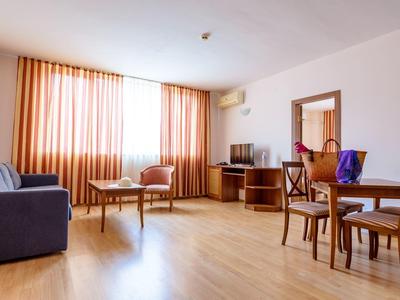 Bright living room with wooden floor, sofa, chairs, and dining table by a window with curtains.