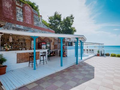 Een open strandbar met blauw-witte meubels naast de zee onder een blauwe lucht.