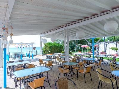 Covered outdoor restaurant area with tables and chairs, view of water in the background.