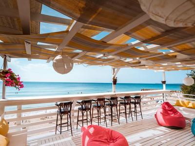 Beach bar with stools, bean bags, and pergola overlooking the ocean.
